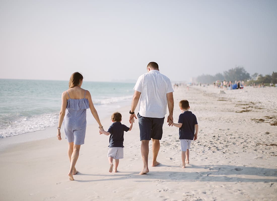 About Our Agency - Rear View of a Family with Two Young Boys Holding Hands While Walking on the Sand on the Beach on a Sunny Day