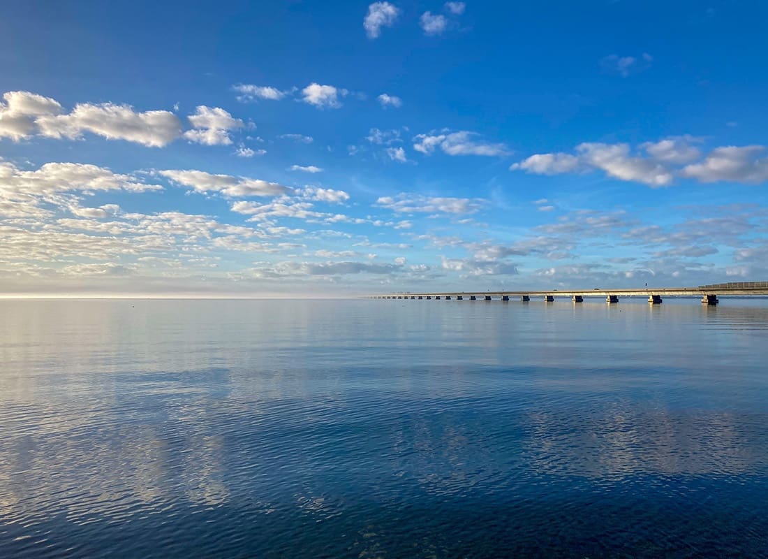 Mary Esther, FL - Scenic View of a Bridge On the Calm Water with a Cloudy Bright Blue Sky in Mary Esther Florida