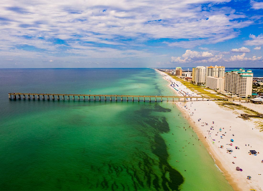 Navarre, FL - Aerial View of a Pier on Turquoise Waters on the Coast in Navarre Florida with Condo and Apartment Buildings in the Distance