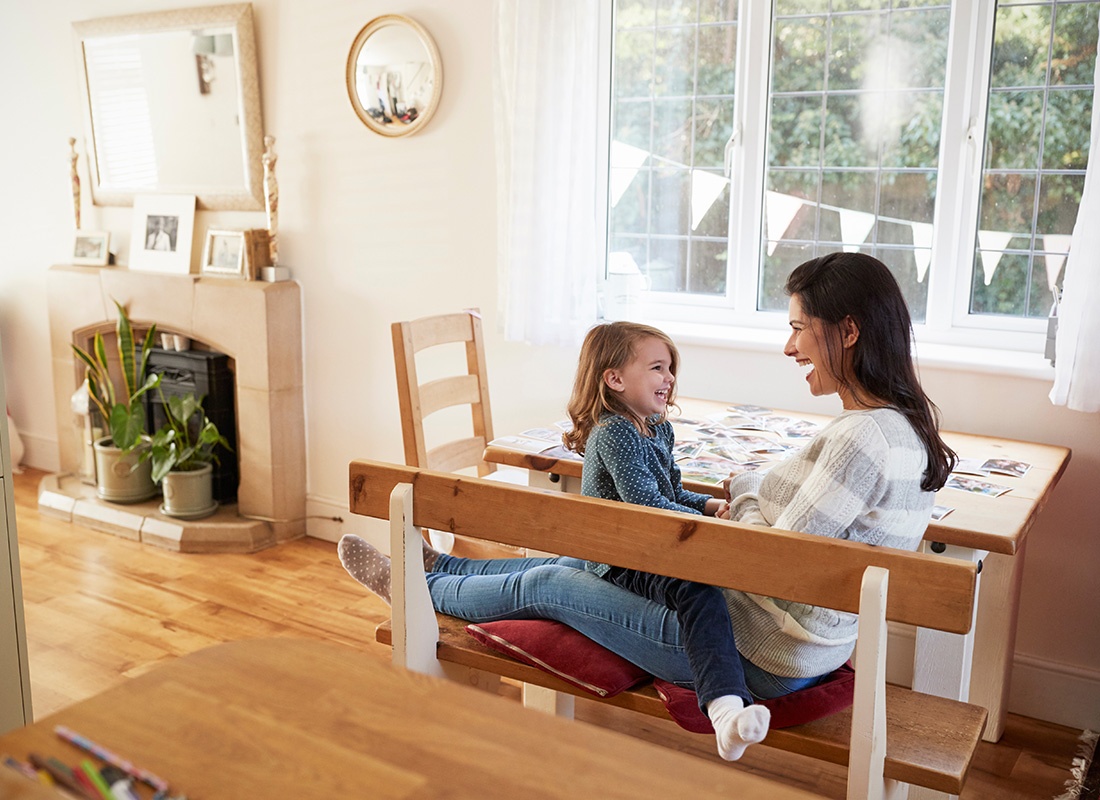 Personal Insurance - Cheerful Mother and Daughter Sitting Together on a Bench in the Dining Room Having Fun Playing Together